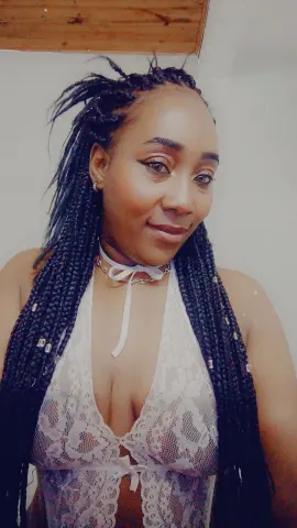 Smiling woman with long black braids wearing a white lace halter top in a bright indoor setting.