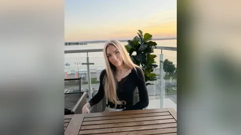 AmiliRay — AmiliRay with long blonde hair sits at an outdoor table overlooking the water during sunset.