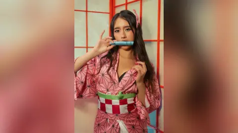 Young woman in pink floral kimono and green obi posing playfully in a traditional Japanese room.