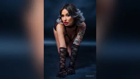Glamorous woman in black lace lingerie and thigh-high stockings posing against a dark moody background.