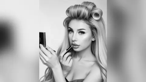 Glamorous blonde woman applying lip gloss in a black and white beauty portrait.