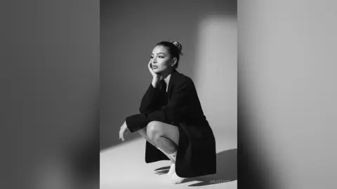 Elegant woman in a black blazer posing thoughtfully in a minimalist black and white studio setting.