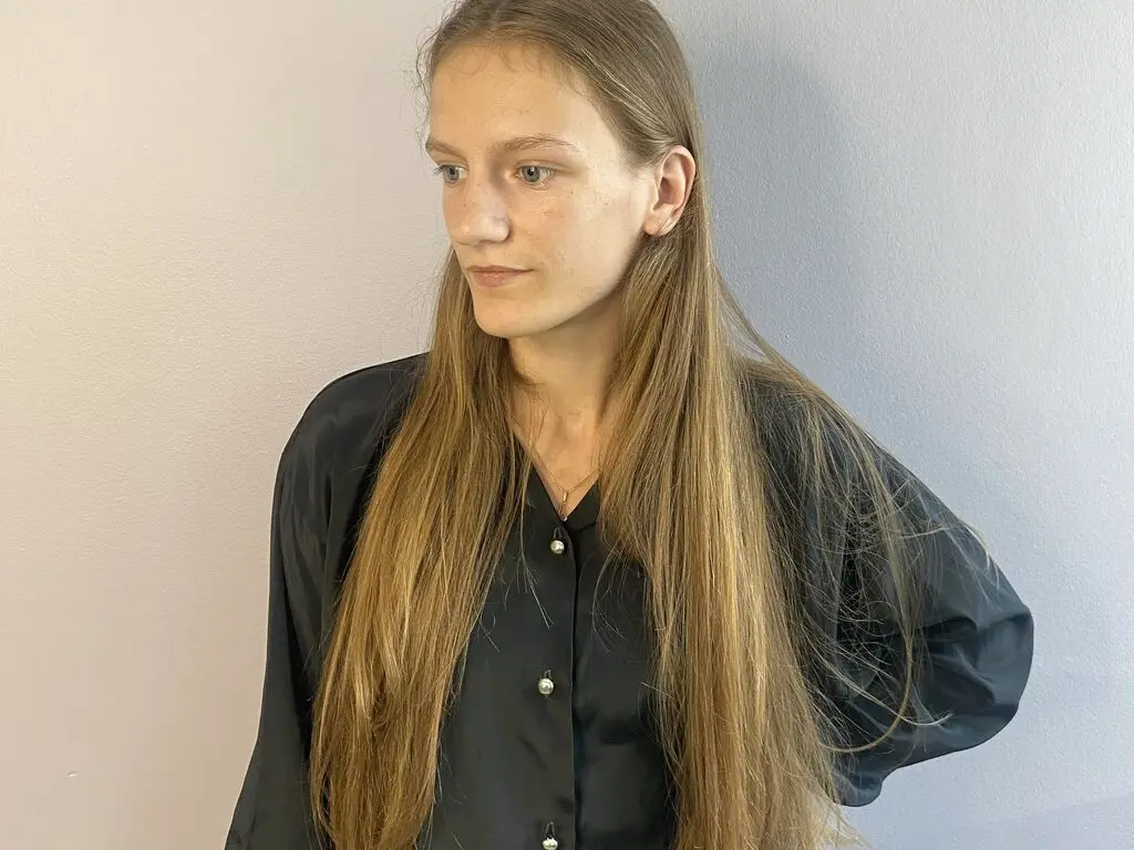 TatumNeild poses with long blonde hair wearing a black button-up shirt against a plain wall.