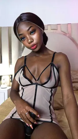 Beautiful Black woman in a beige and black cutout mini dress sitting on a bed in a soft, intimate mood.