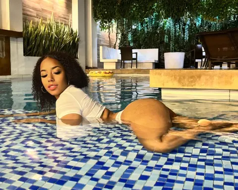 Curvy woman in a white top relaxing in a luxury tiled swimming pool on a sunny day.