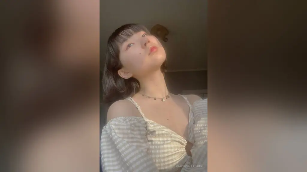 Young woman with short dark hair and bangs wearing a white textured blouse in soft natural sunlight.