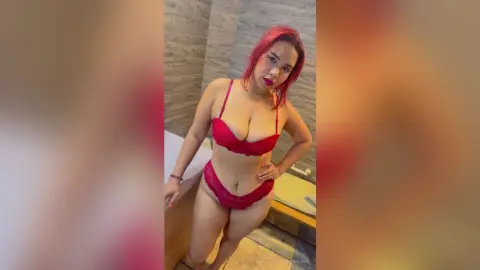 Red-haired woman in red lace lingerie posing confidently in a modern bathroom setting.