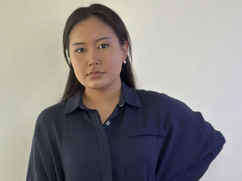 Young woman in a navy blue button-down shirt posing against a plain white wall with a calm expression.