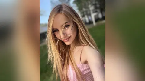 Smiling blonde woman in a pink ribbed tank top wearing gold glasses outdoors in natural sunlight.