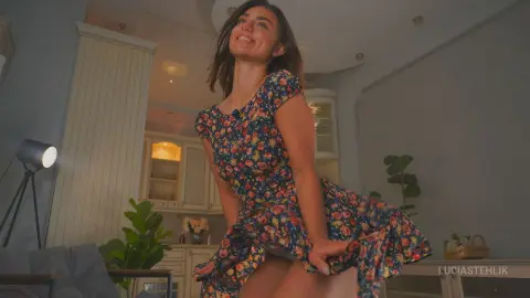Cheerful woman in a floral summer dress laughing in a bright, modern living room setting.