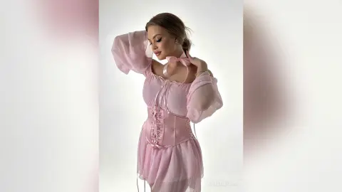 Elegant woman in a romantic pink sheer corset dress posing against a white studio background.