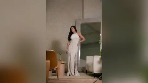 Elegant woman in a white halter neck maxi dress posing in a minimalist modern living room.