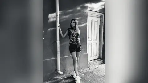 Stylish woman in a graphic tee and shorts leaning against a wall in a moody black and white urban setting.
