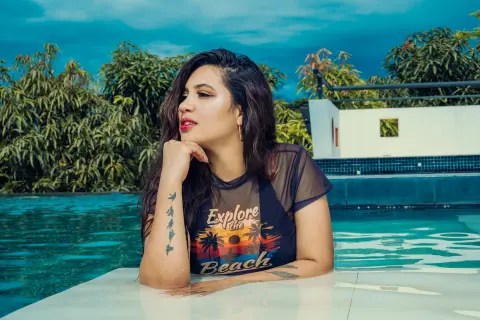 Young woman in a graphic t-shirt relaxing by a luxury swimming pool on a sunny day.