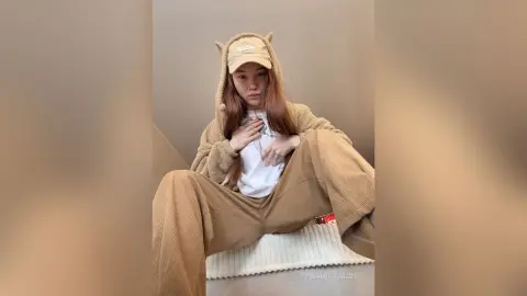 Young woman in cozy tan corduroy loungewear and hooded sweatshirt sitting in a minimalist indoor setting.