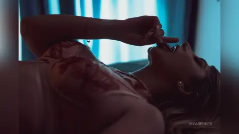 Dreamy close-up of a woman in a floral lace dress relaxing in a dimly lit, moody bedroom setting.