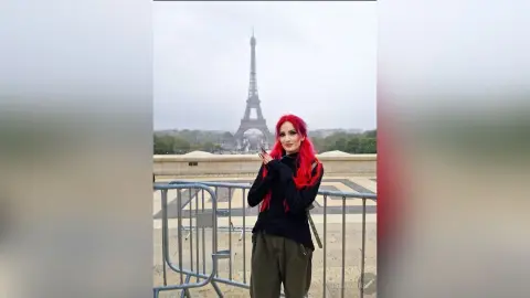 Woman with red hair in a black sweater standing before the Eiffel Tower in Paris on a cloudy day.