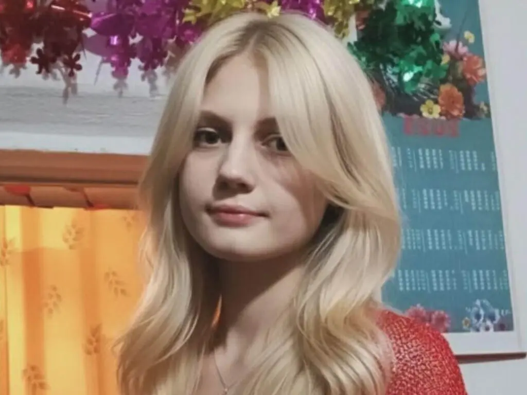 Blonde woman in a red sweater smiling in a room decorated with colorful festive garlands.