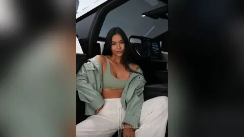 Smiling woman in a sage green jacket and crop top sitting in a modern car interior.