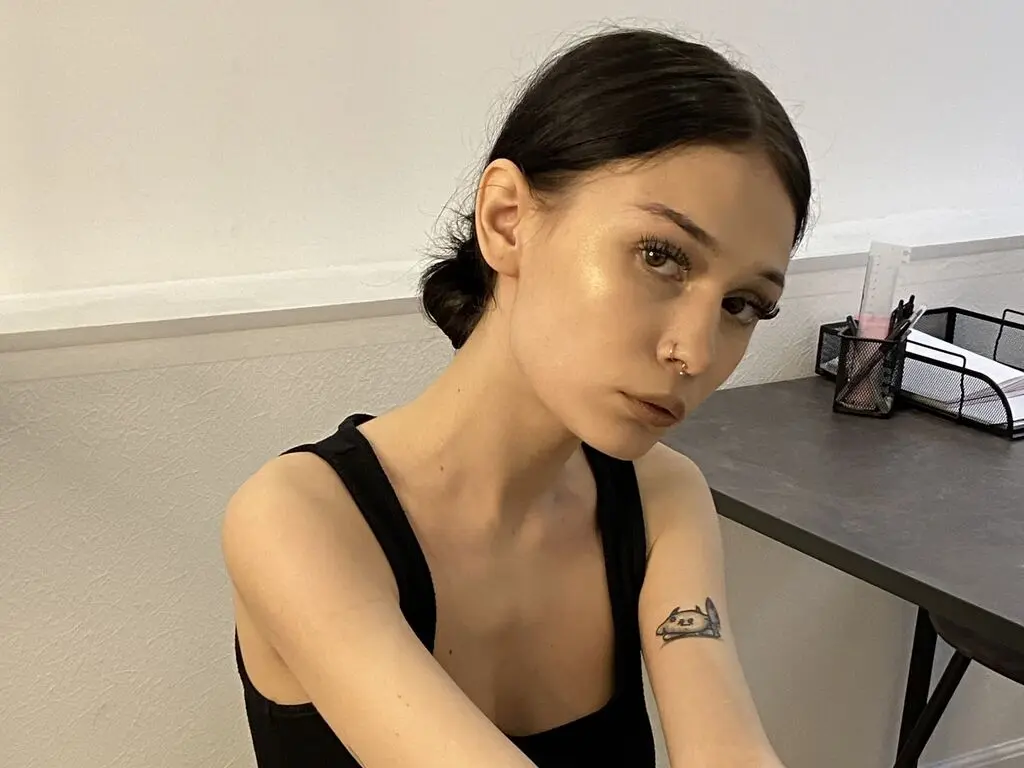 Young woman with dark hair and a black tank top sitting at a desk in a bright indoor setting.
