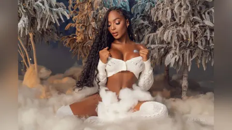 Beautiful woman in a white knit outfit sitting amidst dreamy clouds and frosted winter trees.
