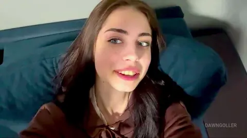 Smiling young woman with long dark hair wearing a brown blouse while relaxing on a blue pillow.