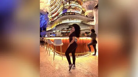 Smiling woman in black casual outfit enjoying a vibrant night at a luxury modern bar with warm lighting.