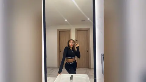 Young woman in black athletic crop top and leggings taking a mirror selfie in a modern minimalist bathroom.