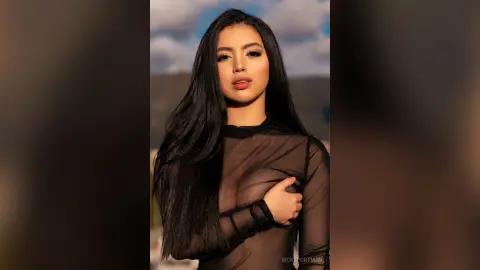 VickyPortman poses in a black sheer long-sleeve top that shows her breasts, with her long black hair falling over her shoulders.