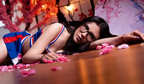 Young woman in a blue sporty crop top lying on a wooden surface surrounded by pink cherry blossoms.
