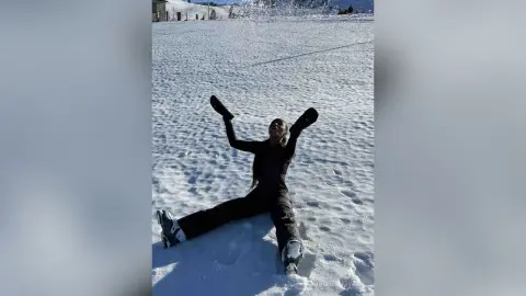 Joyful woman in black winter gear playing in a vast snowy landscape under bright sunlight.