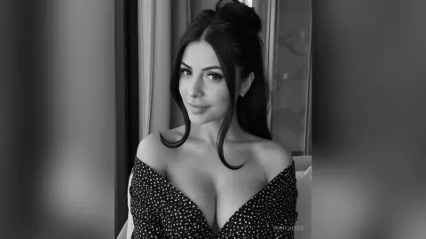 Elegant woman in a black polka dot off-the-shoulder dress posing in a bright indoor setting.