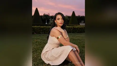 Elegant woman in a cream linen dress sitting on a lawn during a dreamy sunset garden evening.