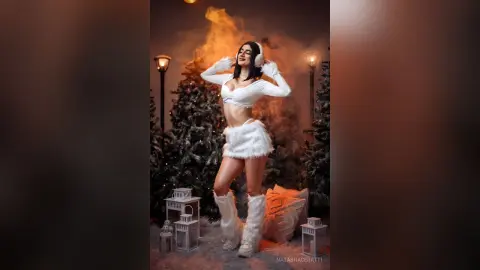 Smiling woman in white winter outfit posing amidst snowy trees and lanterns in a magical festive setting.