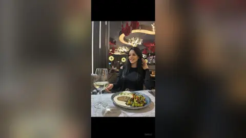 Smiling woman in a black long-sleeve top enjoying a gourmet meal and white wine at a luxury restaurant.