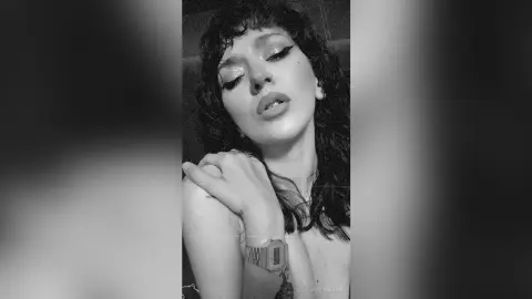 Moody black and white portrait of a woman with wavy hair and glitter eyeshadow looking into the camera.