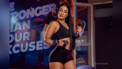 Fit woman in black gym wear lifting dumbbells in a modern fitness studio with a motivational background.