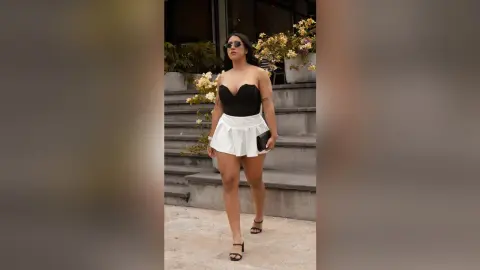 Stylish woman in a black tube top and white mini skirt posing outdoors in a modern urban setting.