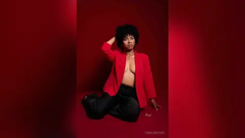 Elegant Black woman in a red blazer and black trousers posing against a bold red background.