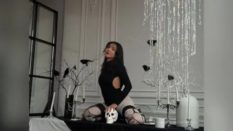 Elegant woman in a black long-sleeve top posing by a crystal chandelier in a moody, sophisticated interior.