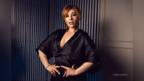 AmeliaReds — AmeliaReds poses in a black silk wrap dress with her hands on her hips against a blue slatted wall.