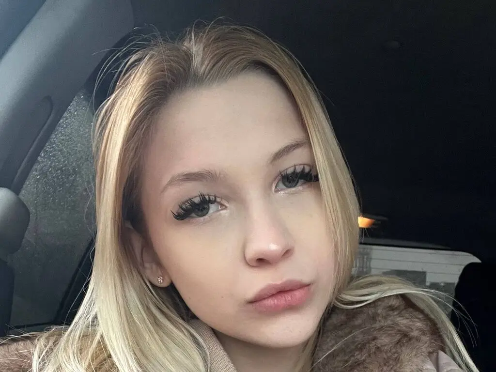 Blonde woman with long eyelashes wearing a cozy brown faux fur coat inside a car at night.