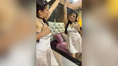 Glamorous woman in a white satin slip dress posing in a luxury bedroom setting with a joyful mood.