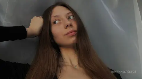 Young woman with long brown hair in a black top posing against a soft grey backdrop with a dreamy mood.