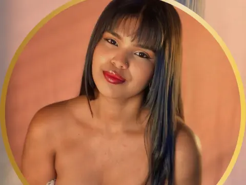 Young woman with long dark hair and red lipstick posing in a warm, soft-lit portrait setting.