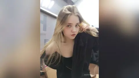 Young woman with long blonde hair wearing a black outfit in a bright indoor setting with a soft mood.