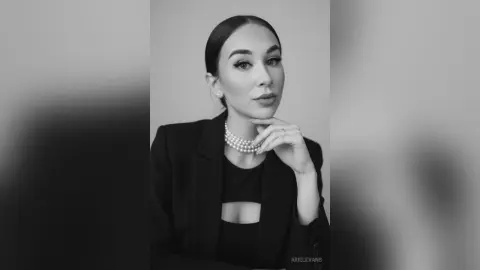 Elegant woman in a black blazer and pearl necklace posing for a sophisticated black and white portrait.