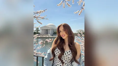 Smiling woman in a patterned top and denim jacket posing by cherry blossoms near the Jefferson Memorial.