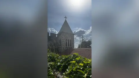 Low angle view of a historic stone church tower under a bright cloudy sky on a sunny day.