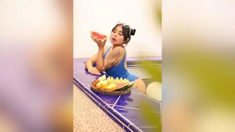 AnneMarcuzzi wears a blue swimsuit while sitting in a pool and eating a slice of watermelon.